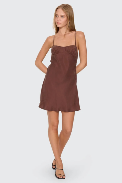 Front standing view of model with hands behind her back wearing the Thrills Elio Bias Mini Dress in Cocoa brown, highlighting the fluid drape and cupro rayon fabric.