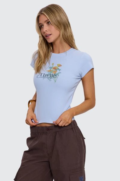 Studio three-quarter front shot of a model wearing a fitted placid blue fine rib tee with yellow floral chest graphics and "Thrills Company" branding, paired with dark brown cargo pants.