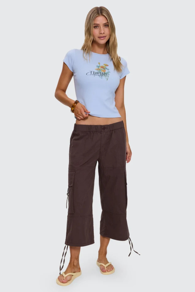 Full-length studio front shot of a model wearing a fitted placid blue floral chest print tee, dark brown cropped drawstring cargo pants, and cream flip-flops.