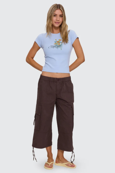 Studio full-length front view of a model posing with hands behind her back wearing a fitted placid blue short-sleeve tee paired with dark brown cropped cargo pants.