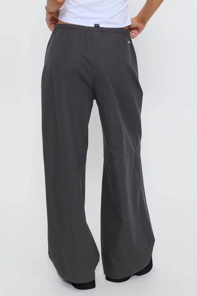 Back view of model wearing the loose straight-leg Thrills Gridlock Ripstop Pant in Charcoal with white crop top and black platform sandals against a plain background.