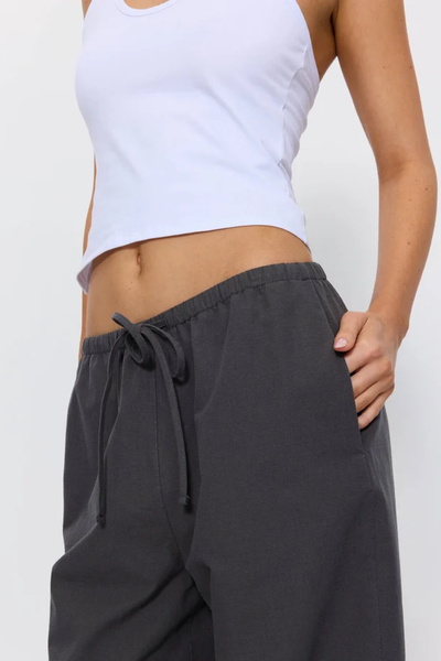 Low-angle front view of model posing in the dark grey Thrills Gridlock Ripstop Pant showcasing the baggy silhouette and drawstring waistband detail.
