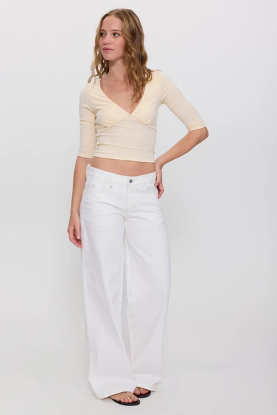 Studio full-length front shot of a model wearing bright white low-rise wide-leg denim jeans paired with a cream V-neck cropped half-sleeve top.