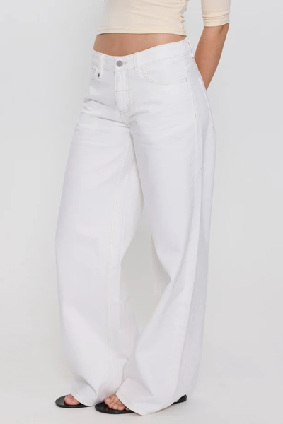 Studio three-quarter side shot from the waist down highlighting the low-rise fit, front fly detail, and wide-leg hem of bright white organic cotton denim jeans.