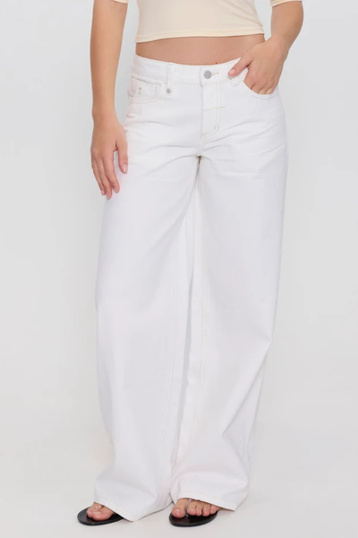 Studio view from the waist down of a model with a hand in her pocket wearing bright white low-rise wide-leg 13.5 oz organic cotton denim jeans.