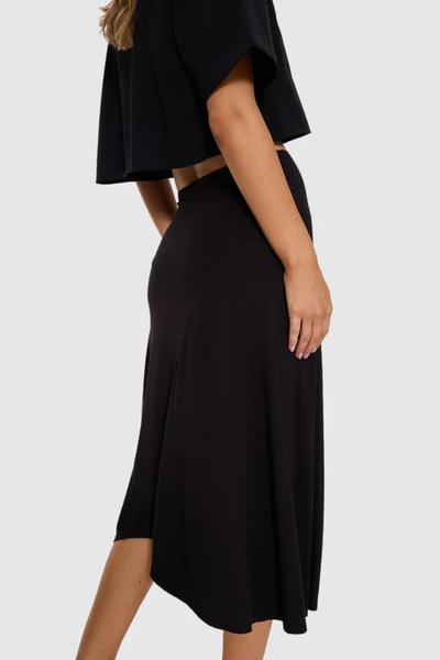 Front lower-body view of model wearing the Thrills Sienna Midi Skirt in Black with a black cropped top and red thong sandals.
