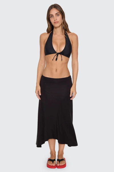 Front lower-body view of model showcasing the asymmetric hemline and fitted silhouette of the Thrills Sienna Midi Skirt in Black.