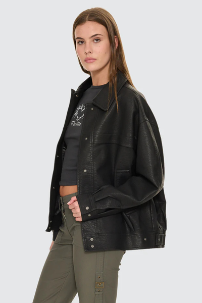 A side-angle view isolating the black oversized jacket on a model, highlighting the loose sleeve volume, dropped shoulder seams, and the deep flap pockets built with clean stitch paneling.