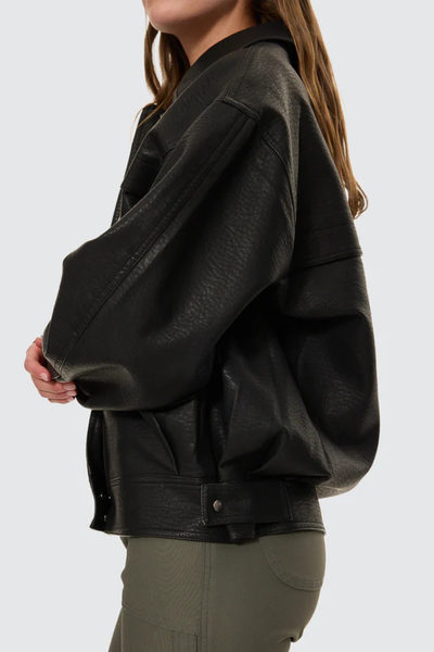A candid outdoor view capturing the model from the side as she walks, highlighting the realistic, lived-in drape of the mid-weight faux leather fabric and its structured look in a real-world setting.