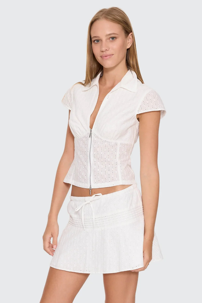 Three-quarter studio view of model posing in the white cotton Thrills Danica Broderie Anglaise Top featuring cap sleeves, a collar, and a zip-front closure.