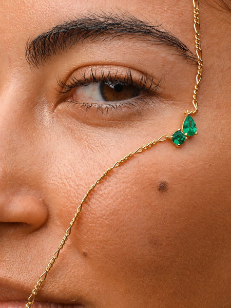 Creative flat lay product shot of the gold necklace artfully draped between two fresh green peppers.