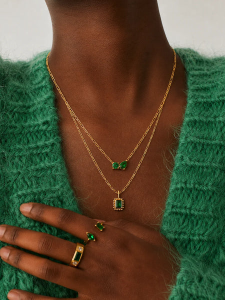 Front-facing studio portrait of a model wearing the emerald Twin Flame necklace centered on her collarbone.