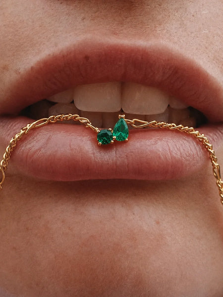 Close-up portrait of a model gently holding the emerald pendant against her lips.