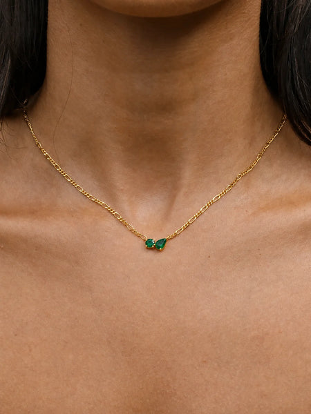 Portrait of a model wearing a textured green cardigan layered with the emerald necklace and a matching emerald pendant necklace.