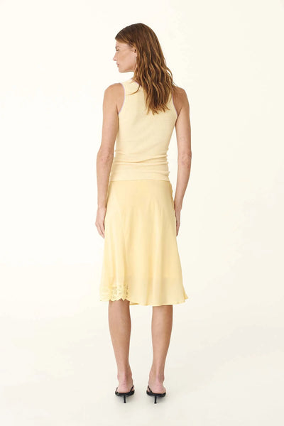 Studio rear view of a model wearing the lemon silk crepe midi skirt paired with a matching yellow top, highlighting the fluid silhouette and asymmetric lace-trimmed hem.