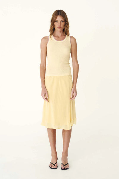 Studio front full-length view of a model wearing the lemon silk crepe midi skirt and a coordinating yellow sleeveless top.