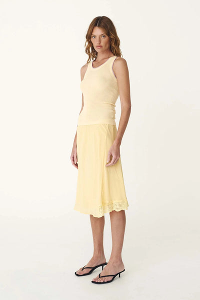 Studio side profile of a model wearing the lemon silk midi skirt, showcasing the mid-length cut and subtle kick at the hem.