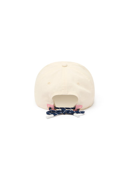A product-only studio shot showing the back profile of The Upside Marlon Soft Cap in cream against a seamless white background. The image clearly displays the soft cotton panels, embroidered ventilation eyelets, and the adjustable navy paracord tie detailed with pink trim and gold eyelets.
