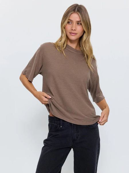 Studio photo of a model wearing the Thrills Hemp Square Tee in Falcon brown, holding the hemline to demonstrate the soft hemp-cotton jersey fabric and relaxed fit.