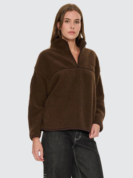 A full-length product shot from the back on a model wearing the brown sherpa jumper, emphasizing the cropped streetwear silhouette, drop shoulder alignment, and the continuous black contrast binding running along the bottom waist edge.