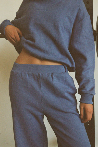 A mid-section lifestyle shot focusing on the high-rise fit of the blue sport sweatpants, detailing the clean front rise and structural gathering of the fine-ribbed elastic waist.