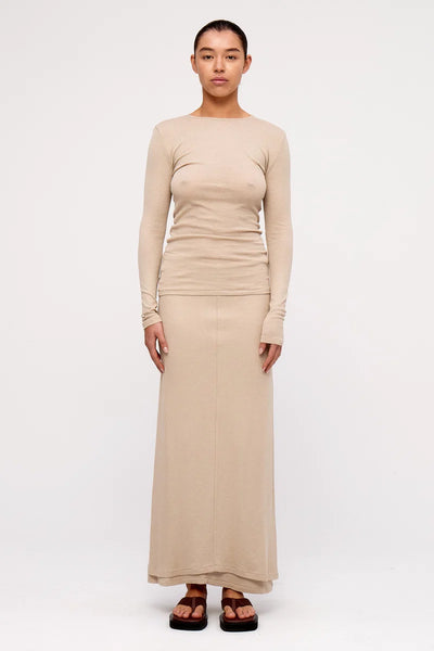Full-length front view of a model wearing the slim-fit Zulu & Zephyr Rib Hemp Jersey Long Sleeve Top in husk beige, paired with a matching maxi skirt and brown sandals.