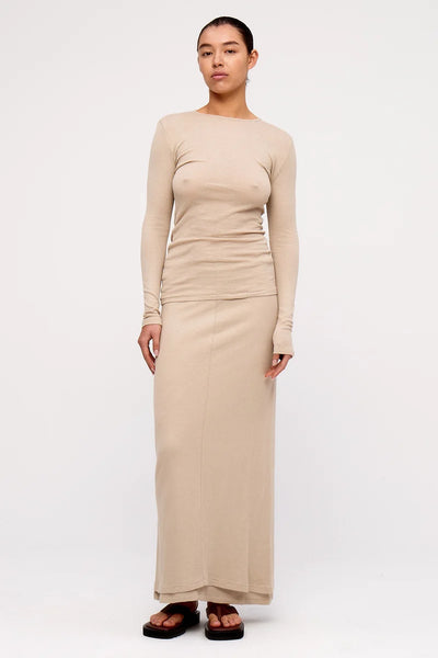 Full-length front view of a model wearing the slim-fit Zulu & Zephyr Rib Hemp Jersey Long Sleeve Top in husk beige, paired with a matching maxi skirt and brown sandals.