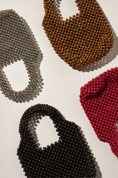 A flat lay composition showing four colorways of the petite purse—silver, black, deep red, and walnut brown—arranged together on a white surface to highlight the distinct textures and finishes across the collection.