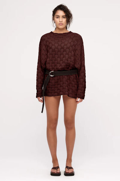 A full-length front studio image showcasing the basketweave sweater styled with a wide dark belt at the waist, emphasizing its multi-functional design and styling adaptability.