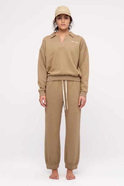 A full-length front studio shoot of a model wearing the olive collared sport sweatshirt and matching cuffed sweatpants, highlighting the structured look of the open collar neckline, ribbed waistband, and small white embroidered chest logo.