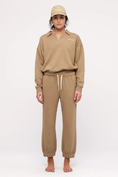 A full-length studio shot of the olive cuffed sport sweatpants styled casually with a matching olive short-sleeve t-shirt, highlighting the functional side seam pocket placement with a hand tucked inside.