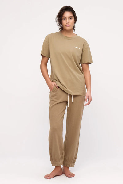 A full-length studio shot of the olive cuffed sport sweatpants styled casually with a matching olive short-sleeve t-shirt, highlighting the functional side seam pocket placement with a hand tucked inside.