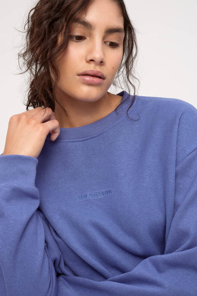 A close-up studio shot detailing the upper half of the blue sport sweatshirt, showcasing the fine-ribbed crew neckline, dropped shoulders, and the centered, color-matched tonal embroidered "ZULU & ZEPHYR" logo.