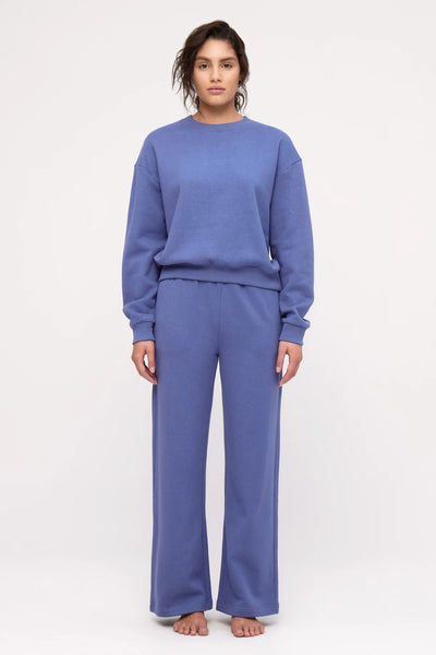 A full-length front-facing studio shot of a model wearing the blue mid-weight fleece sweatshirt and matching wide pants, showcasing the relaxed, oversized silhouette and ribbed cuffs and hem.