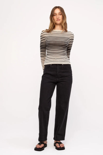 Full-length studio photo of a model featuring the long-sleeve Zulu & Zephyr Ramie Cotton Knit Top in Ombre Stripe with hands behind her back, paired with black denim.