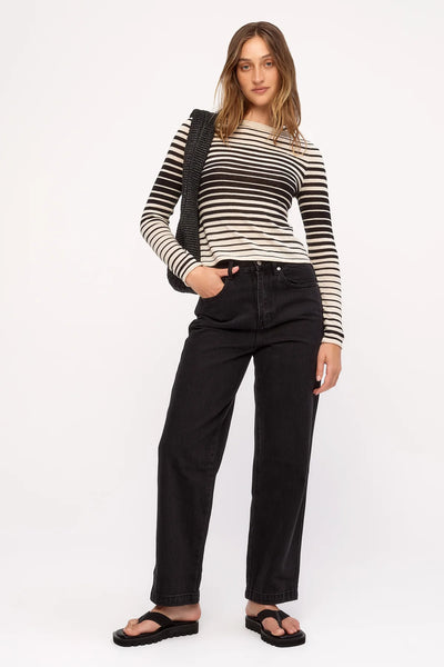 Full-length studio shot of a model wearing the high-neck Zulu & Zephyr Ramie Cotton Knit Top in Ombre Stripe, styled with black denim jeans, black slides, and a black woven shoulder bag.