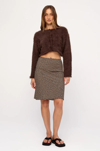 Front studio view of a model featuring the long-sleeve, cropped Zulu & Zephyr Fully Knit Cardigan in Chocolate paired with a brown printed skirt and platform sandals.