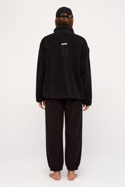 Back view of a model wearing the oversized Zulu & Zephyr Black Sherpa Jacket, showcasing the high fleece collar and the small white embossed logo patch on the upper back panel.