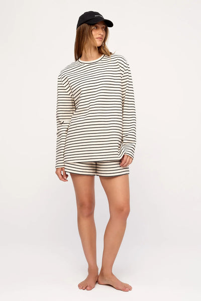 Full-length studio shot of a model wearing the relaxed-fit Zulu & Zephyr Jersey Long Sleeve Top in Black Stripe paired with matching striped shorts and a black cap.