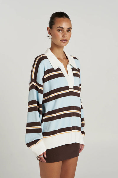 A side-profile studio product angle of the long-sleeve knit polo, demonstrating the cozy drape of the 16-gauge soft organic cotton fabric and the fluid continuity of the multi-colored stripe pattern down the arm.