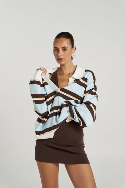 A three-quarter studio portrait of a model crossing her arms while wearing the relaxed-fit knit polo sweater, showcasing how the loose drop-shoulder style layers effortlessly over basic tops.