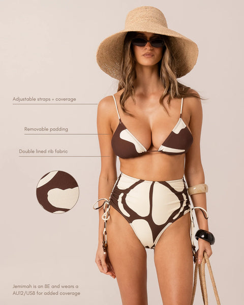 Studio front three-quarter view of model Yasmin wearing sunglasses and the chocolate brown underwire one-piece swimsuit with adjustable side ruching.