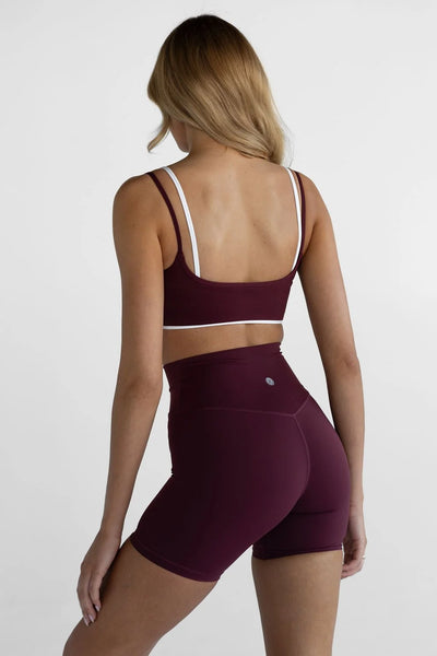 Back view of a model wearing the Leelo Double Layer Crop Top in Cherry Cola, highlighting the white inner spaghetti straps and white trim on the under-bust band paired with matching shorts.