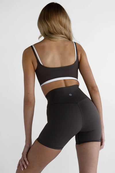 Back view of a model wearing the Leelo Double Layer Crop Top in Dark Chocolate, highlighting the white inner spaghetti straps, scoop back, and white under-bust trim paired with high-waisted bike shorts.