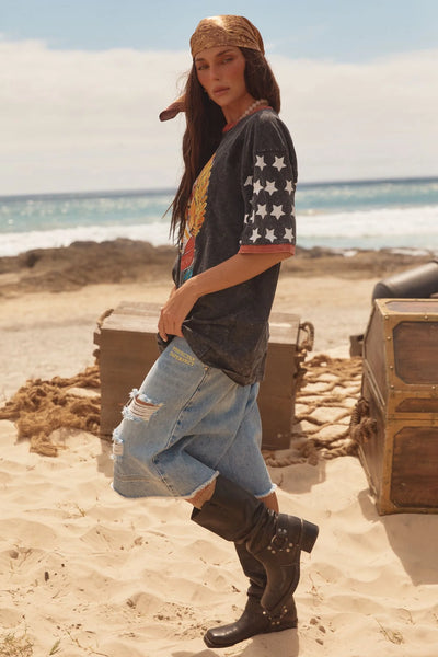 A side-angle studio product shot isolating the washed black cotton tee on a model, emphasizing the dramatically dropped shoulder seams, extra-long slouchy fit, and the high-density star spangle sleeve prints.