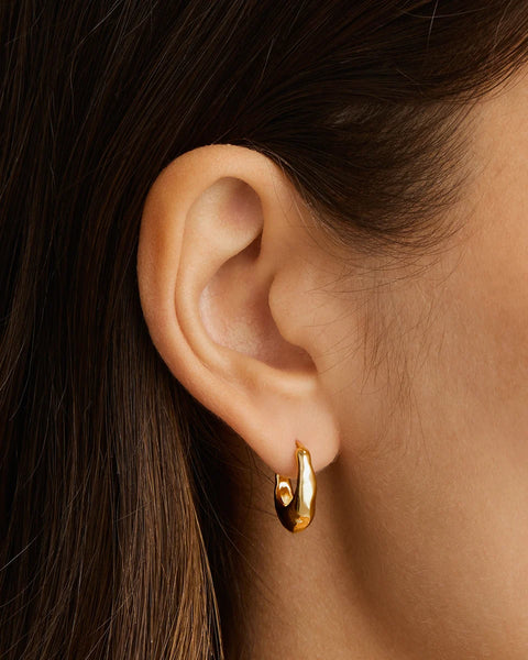 A close-up of a model's ear wearing a small gold huggie hoop earring.