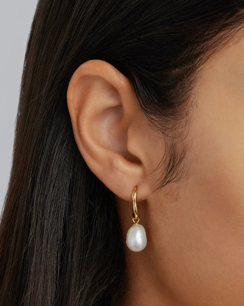 Close-up view of a model wearing a By Charlotte 18k Gold Vermeil Harmony Pearl Hook Earring, featuring an organic baroque freshwater pearl drop attached to a curved gold hook.