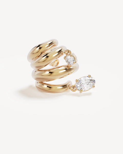 Close-up product shot of a single By Charlotte In the Stars Illusion Hoop in 18k gold plating showing the multi-band ribbed curve with dangling round and oval cubic zirconia stones.