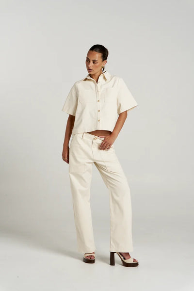 Full-length studio view of a model wearing the full Summi Summi Carpenter set in Ecru, featuring the short-sleeve button-down shirt paired with high-waisted carpenter pants and platform heels.