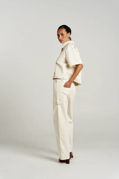 Side profile view of a model in the Ecru Summi Summi Carpenter SS Shirt and matching utility pants with hands in back pockets.